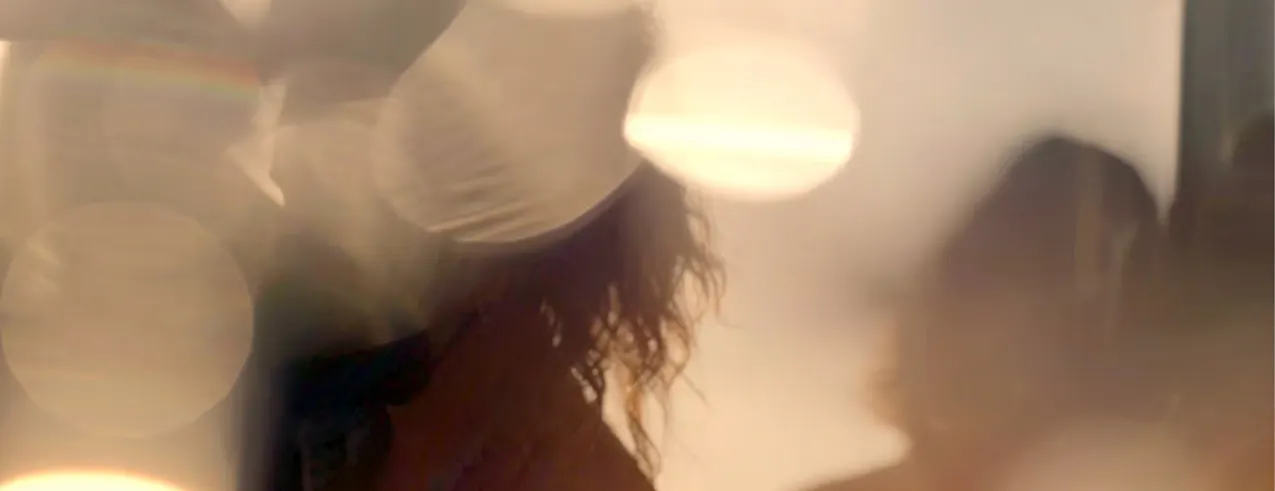Portrait artistiquement flou avec des reflets de lumière et une mise au point douce, montrant vaguement une personne avec des cheveux ondulés