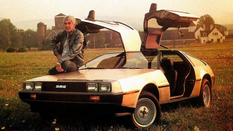 De Lorean DMC in argento, John De Lorean appoggiato all'auto, portiere aperte, piccolo villaggio sullo sfondo