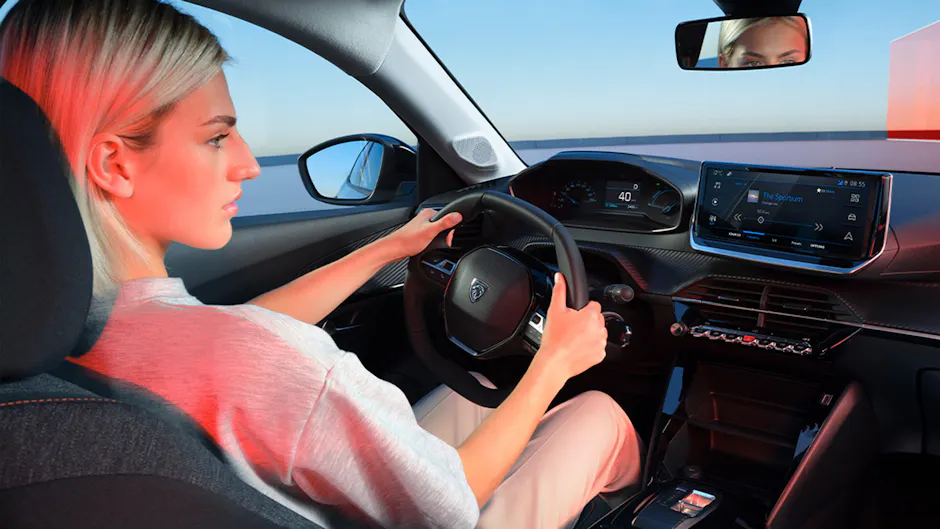 Dame au volant de la Peugeot E-208, vue intérieure sur le cockpit