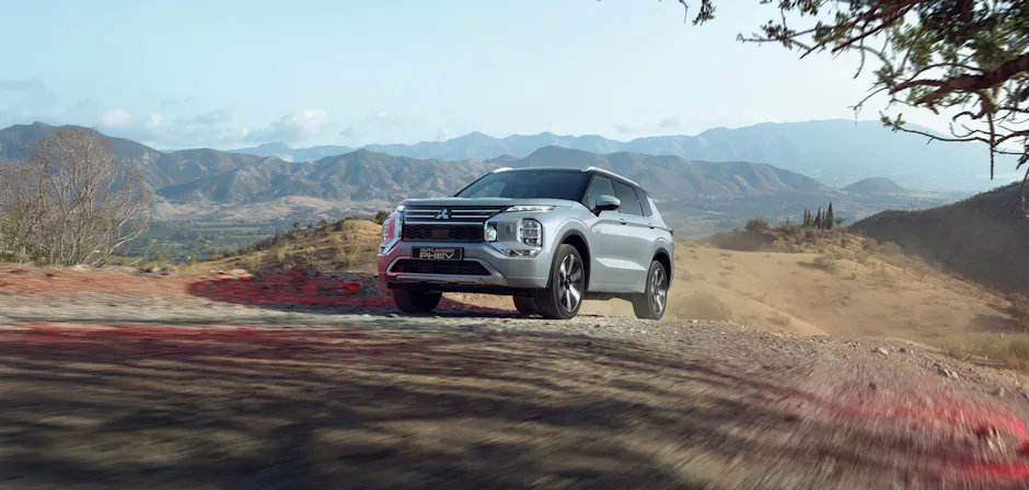 Mitsubishi Outlander grigio fuoristrada, paesaggio montano e strada sterrata