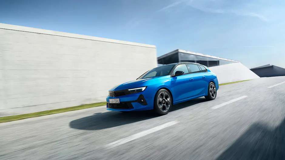 Opel Astra in blu come ibrida plug-in, cielo blu ed edifici in cemento armato