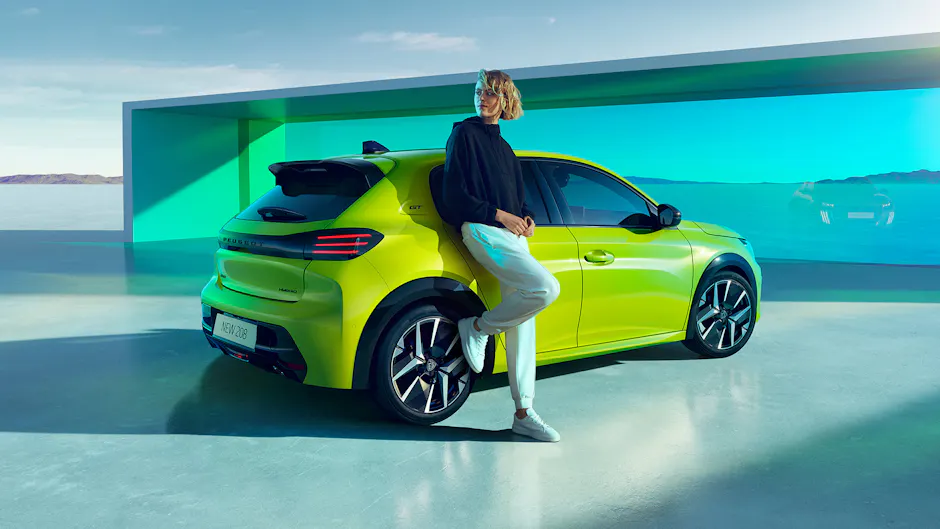 Peugeot E-208 jaune de l'arrière, femme appuyée contre l'aile