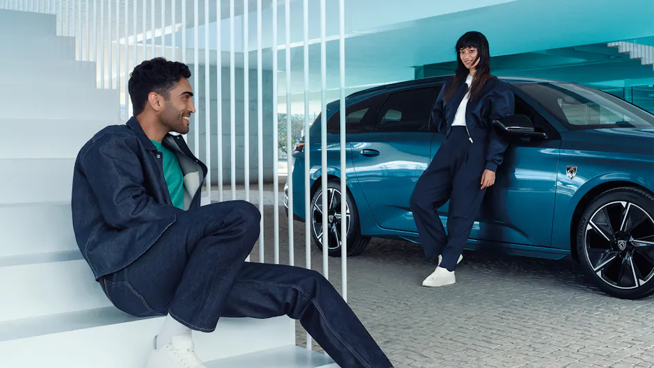 Uomo seduto sulle scale, Peugeot 308 SW sullo sfondo e donna appoggiata all'auto