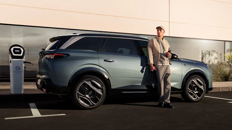 Peugeot E-5008 à la station de recharge, homme en attente adossé au véhicule