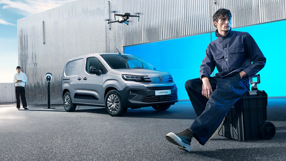 Peugeot E-Partner est chargé en arrière-plan, un drone filme une personne sur une valise