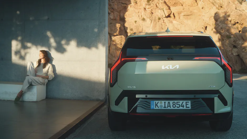 Kia EV3 von hinten, Frau auf Bank im Hintergrund