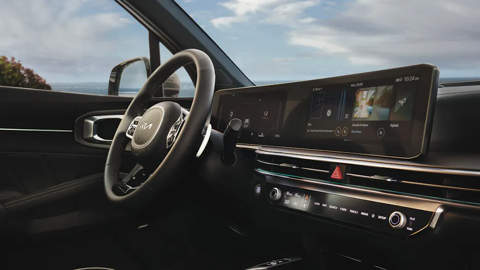 Interni della Kia Sorento in nero, grande display, cielo blu con qualche nuvola