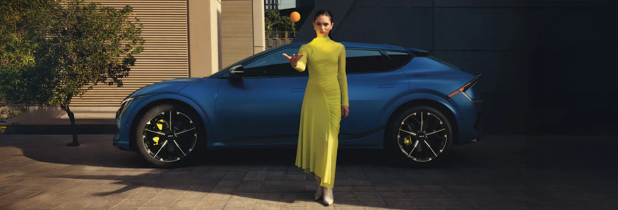 Kia EV6 GT bleue à l'arrière plan, modèle en robe jaune devant