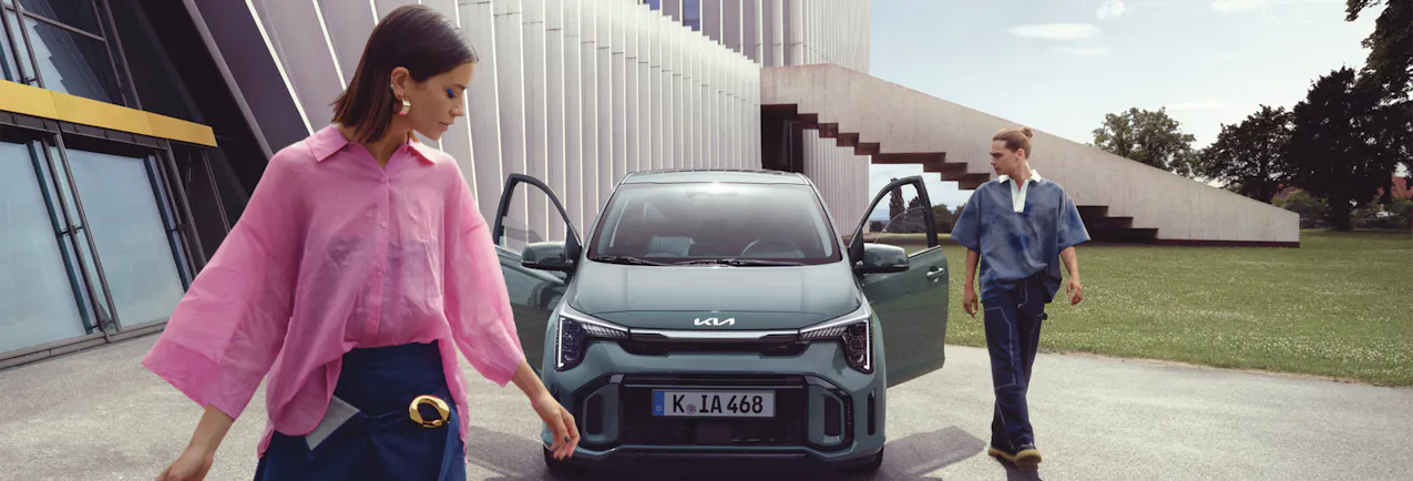 Kia Picanto davanti a un edificio moderno, 2 modelli davanti al veicolo