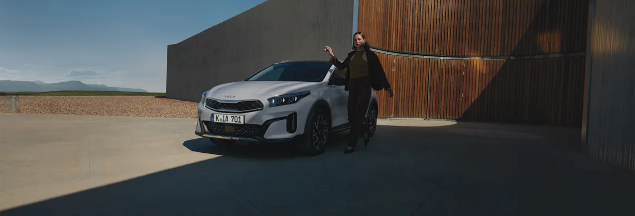 Kia XCeed in Weiss, eine stillvolle Frau neben dem Auto, ein modernes Gebäude mit blauem Himmel
