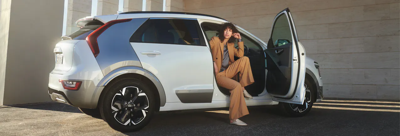 Kia Niro di colore bianco con portiere aperte, donna elegante in auto