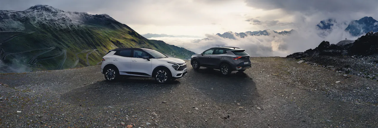 Due Kia Sportage in bianco e grigio su un passo di montagna, in un mare di nuvole e sole