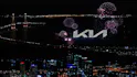 Logo Kia entouré de feux d'artifice, grande ville avec beaucoup d'éclairage tout autour