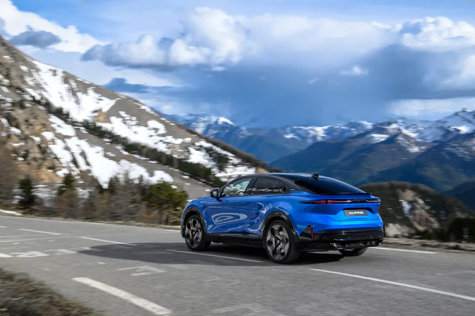 Alpine A390 GTS in vista dinamica laterale mentre percorre una curva stretta su una strada di valico alpino con panorama montano