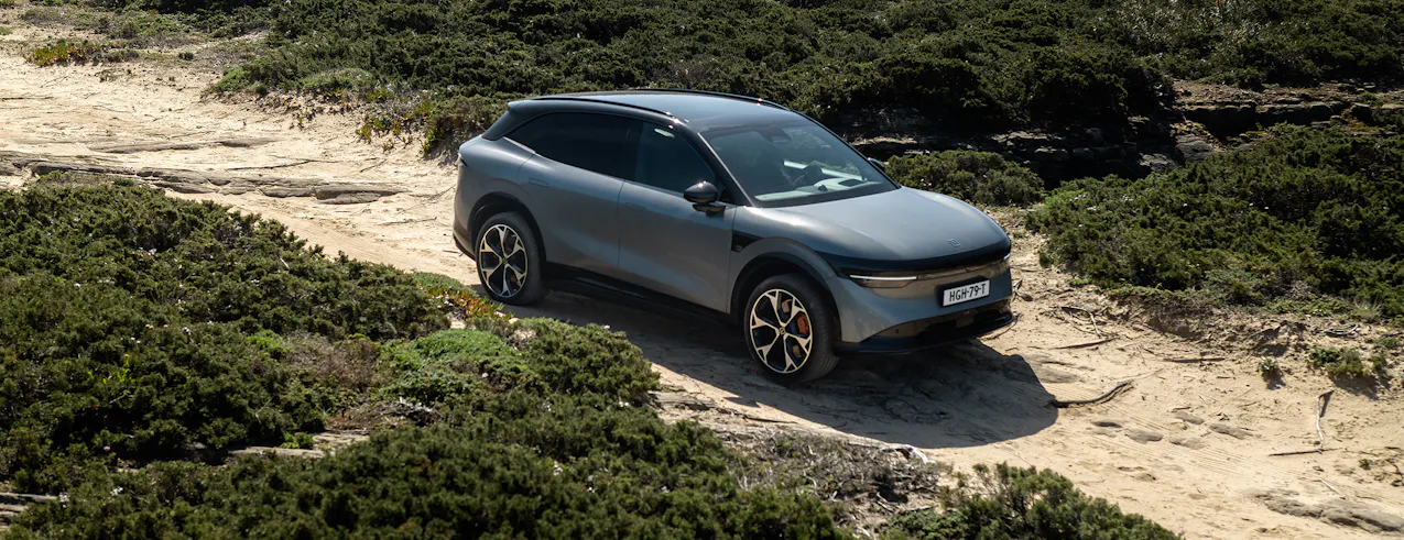Zeekr 7X in Tech Grey, su una strada costiera sabbiosa, circondata da cespugli