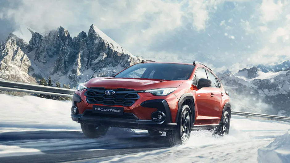 Subaru Crosstrek rosso su una strada di montagna con neve, montagne innevate sullo sfondo