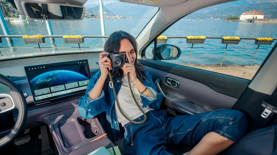 Una donna è seduta su una Leapmotor e scatta una foto con la macchina fotografica, sullo sfondo si vedono un lago e delle montagne.