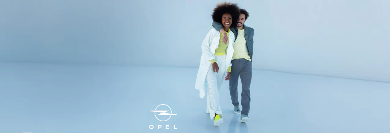 Couple souriant vêtu de tenues sportives tendance dans une pièce lumineuse et minimaliste ; en bas à gauche, le logo Opel.