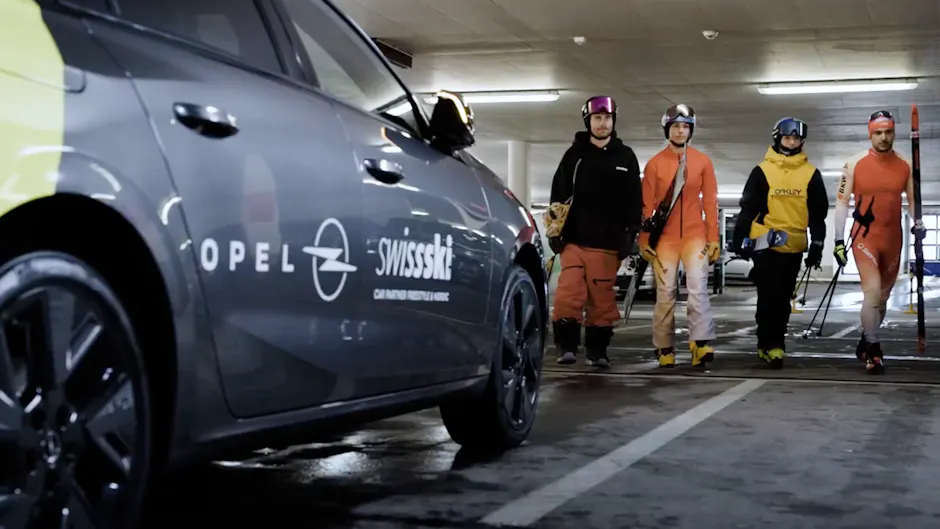 Una Opel grigia, sullo sfondo due sciatori, uno snowboarder e un fondista.