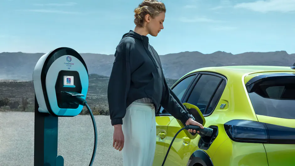 Au centre, une femme recharge sa Peugeot jaune vif dans le désert.