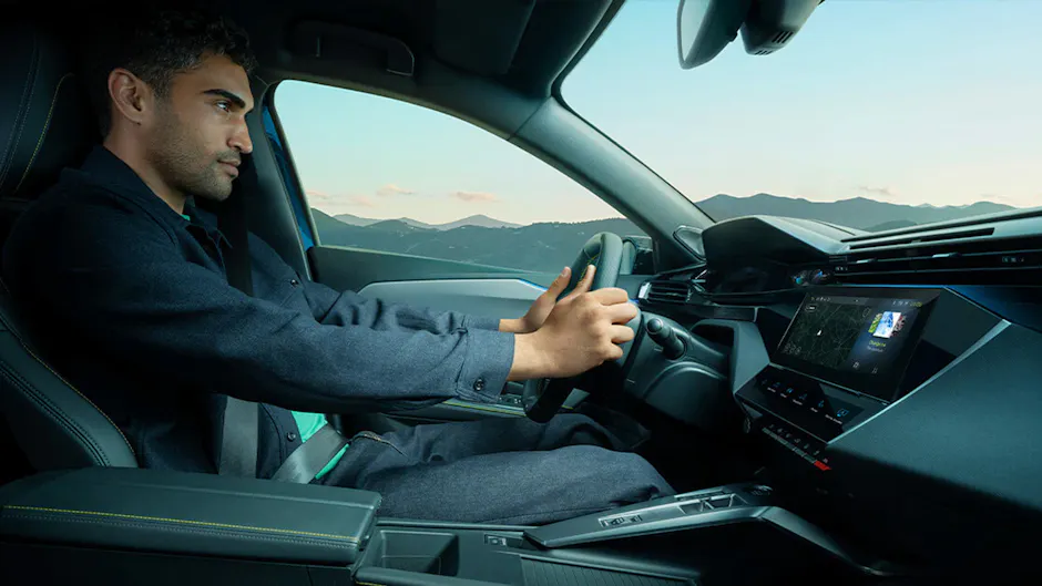 Homme au volant d'une voiture, avec des montagnes et des nuages en arrière-plan.