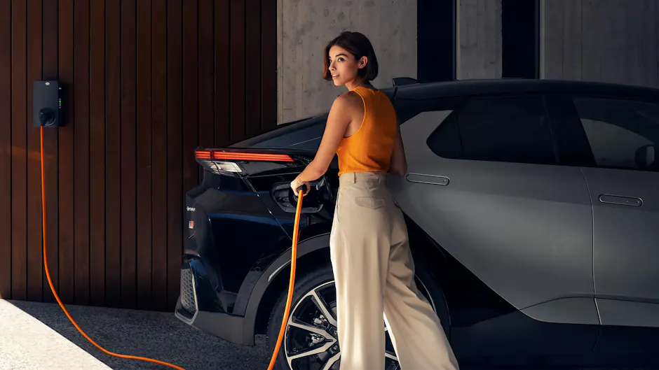 Une femme vêtue d'un haut orange branche sa Toyota à l'électricité.