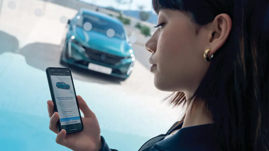 Une femme utilise l’application MyPeugeot et, en arrière-plan, se trouve une Peugeot