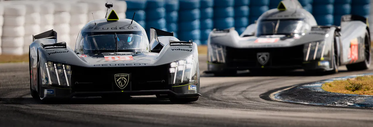 Deux voitures de course Peugeot roulent sur un circuit, la voiture de tête porte le numéro 93