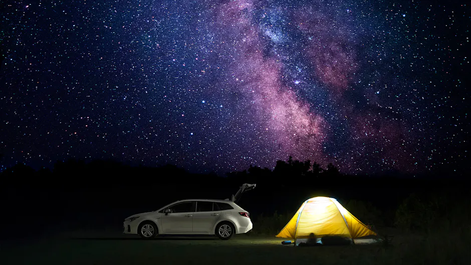 Suzuki blanche avec tente jaune sous un ciel étoilé