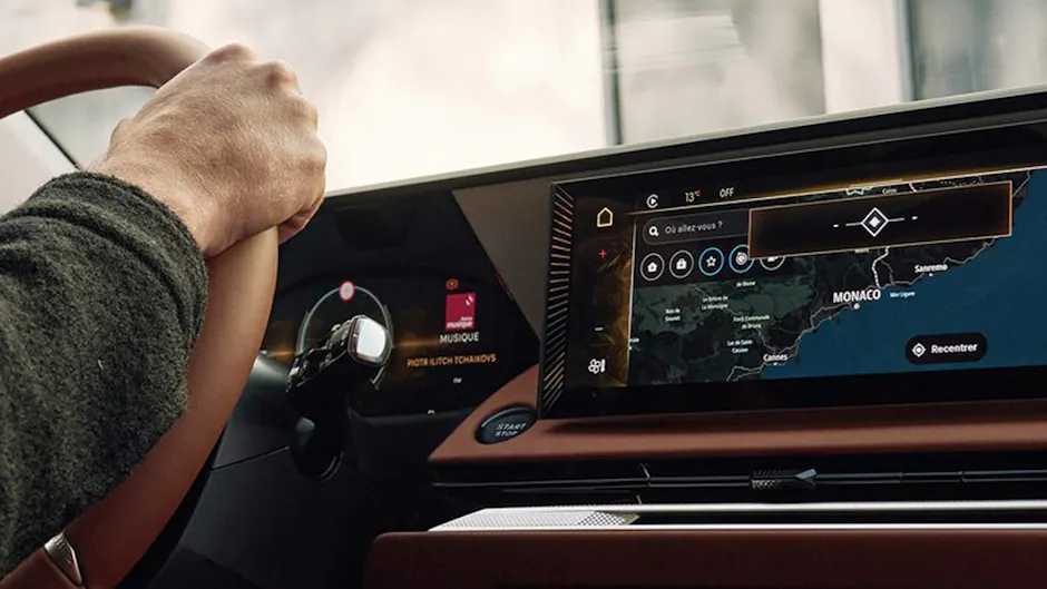 Une personne conduit une DS Automobiles, dont l'intérieur est de couleur marron ; l'écran affiche la carte de navigation