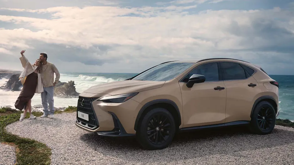 Une Lexus NX vue de profil ; à gauche, un couple prend un selfie ; en arrière-plan, la mer avec des vagues