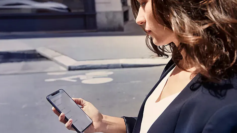 Une femme regarde son téléphone portable, avec une rue en arrière-plan