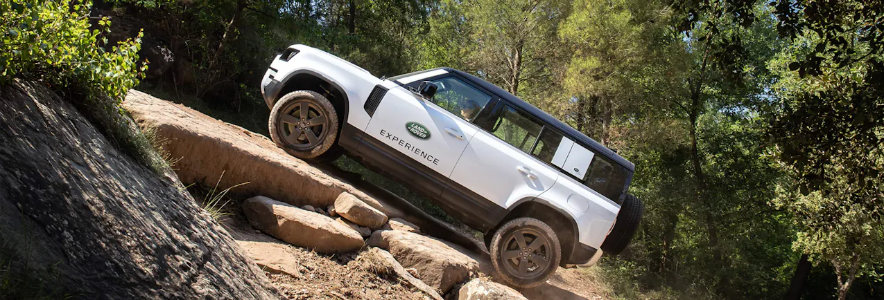 Land Rover Defender bianca vista di lato, mentre sale lungo un sentiero sassoso