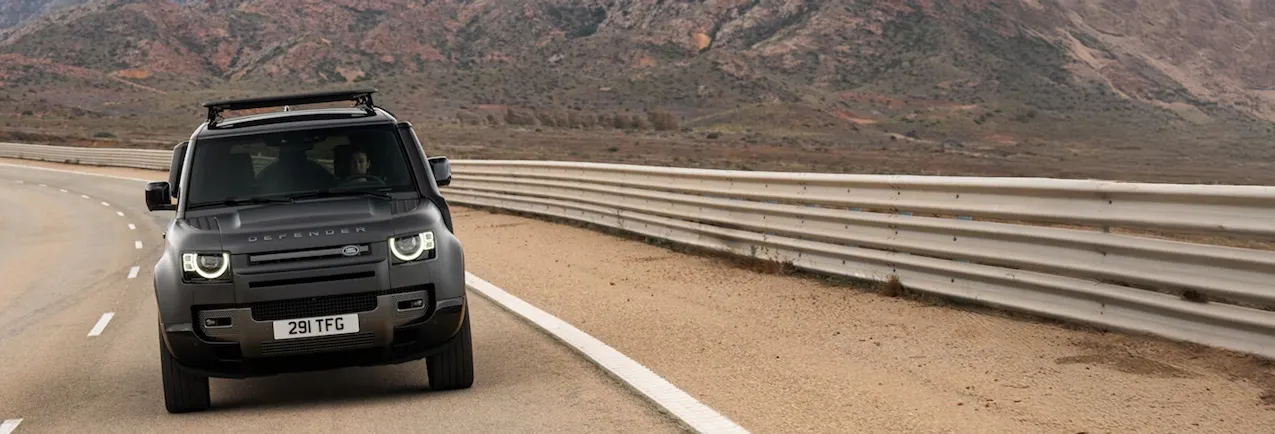 Land Rover Defender nera vista di fronte, mentre percorre una strada; sullo sfondo si vedono delle colline
