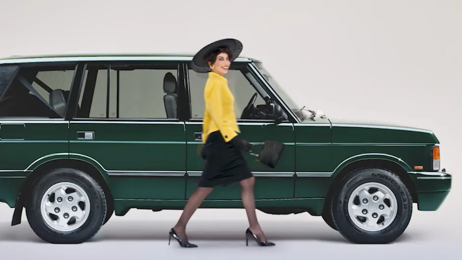 Vecchia Range Rover di un elegante colore verde, una donna corre davanti all'auto