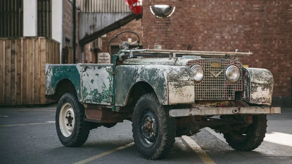 Ein alter Land Rover in Grün, steht vor einer Backsteinwand