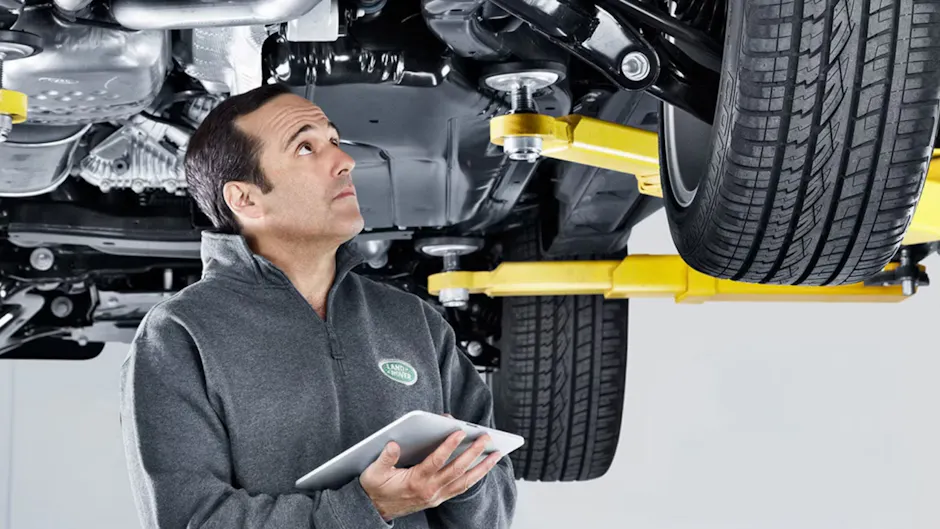 Employé Land Rover avec liste de contrôle sous un véhicule haut de gamme 