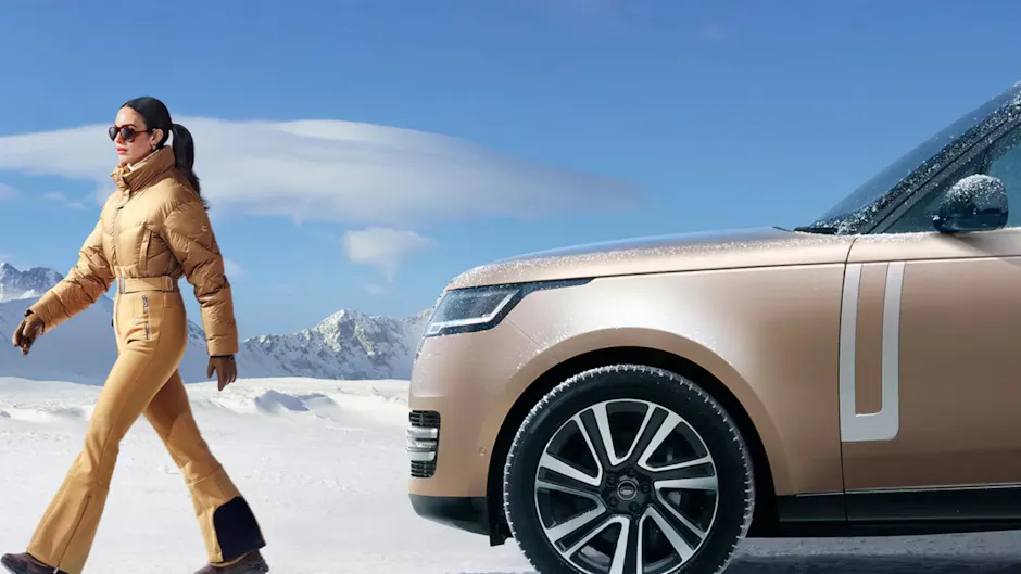Ein Range Rover im Schnee, eine Frau läuft vom Auto weg, blauer Himmel im Hintergrund mit einer Wolke