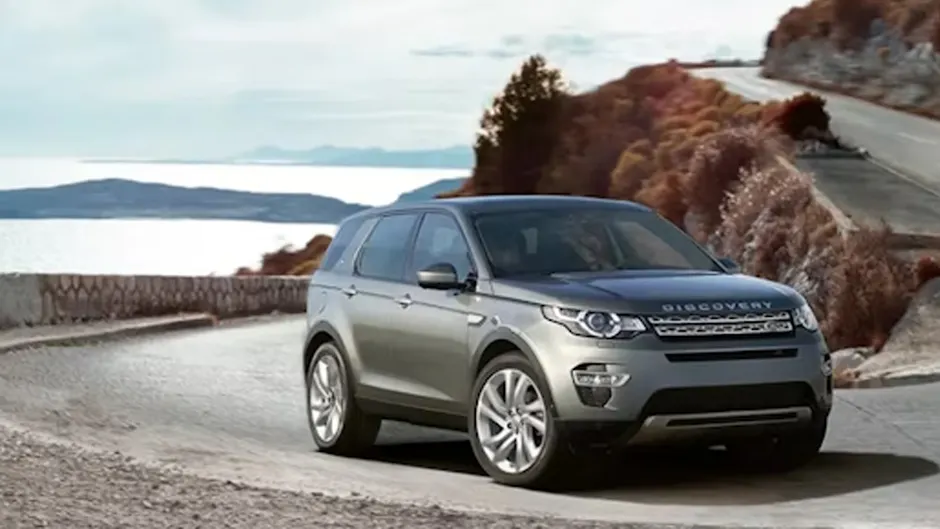 Ein silbrigen Land Rover Discovery, fährt auf einer Küstenstrasse, im Hintergrund das Meer