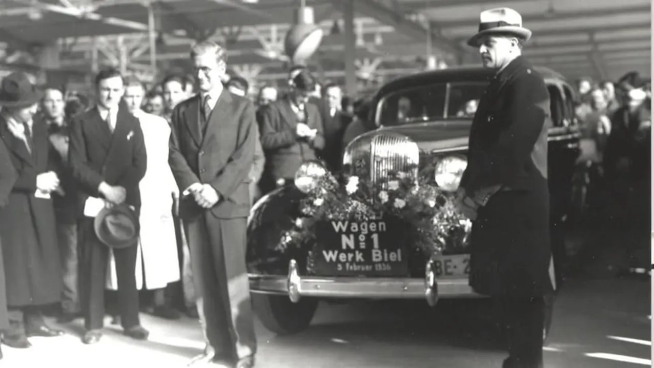 Photo en noir et blanc montrant de nombreuses personnes présentant la première voiture de l'usine de Bienne. 
