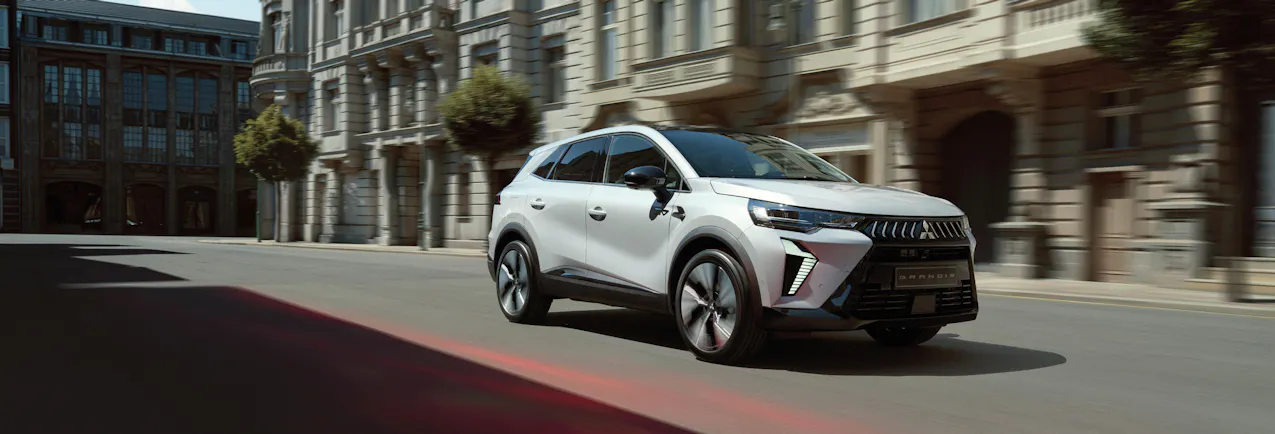 Une Mitsubishi Grandis roule dans une ruelle bordée de vieilles maisons 