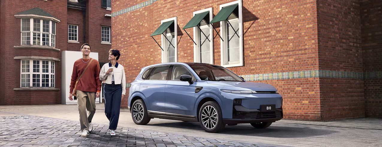 Leapmotor B10 in elegante blu, davanti a un muro di mattoni, un uomo e una donna che si allontanano correndo dall'auto