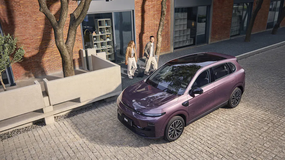 Leapmotor B10 in un elegante colore viola, accanto a una casa in mattoni, un uomo e una donna corrono verso l'auto.