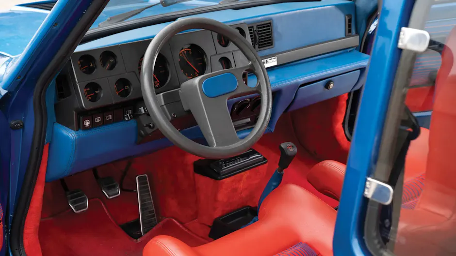 Abitacolo della Renault 5 Turbo con interni blu e rossi e un volante asimmetrico a forma di L.