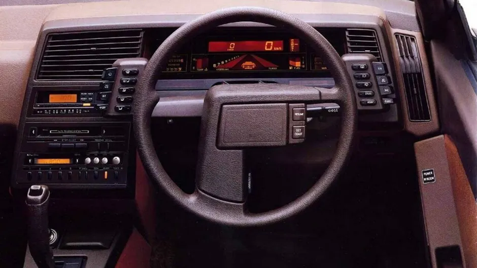 Interni di una Subaru XT con volante rettangolare, display digitale e numerosi pulsanti sul cruscotto.