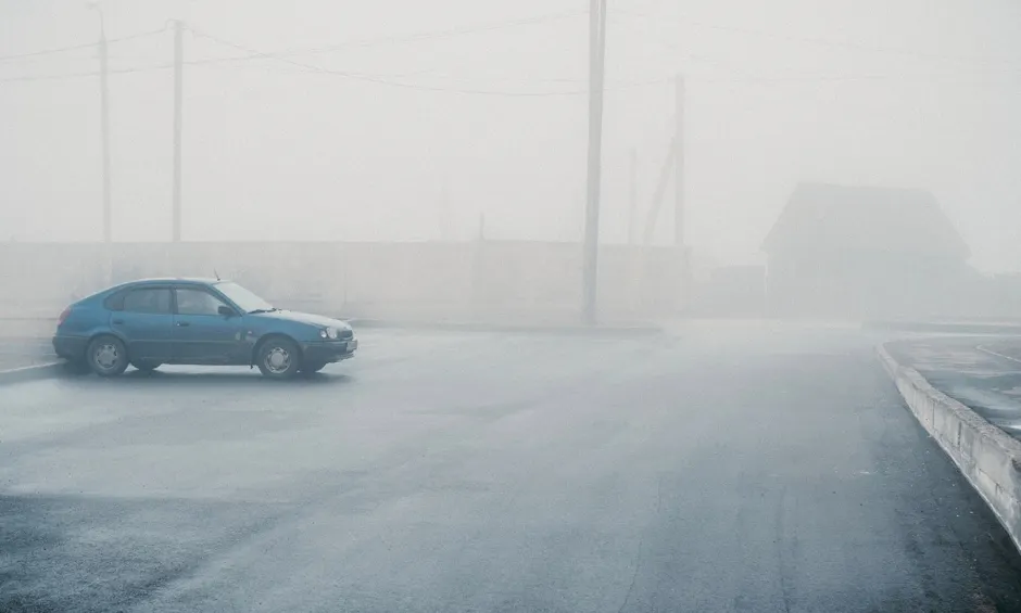 Auto auf Landstrasse in dichtem Nebel, eingeschränkte Sichtweite, herbstliche Stimmung mit unscharfer Silhouette im Hintergrund.