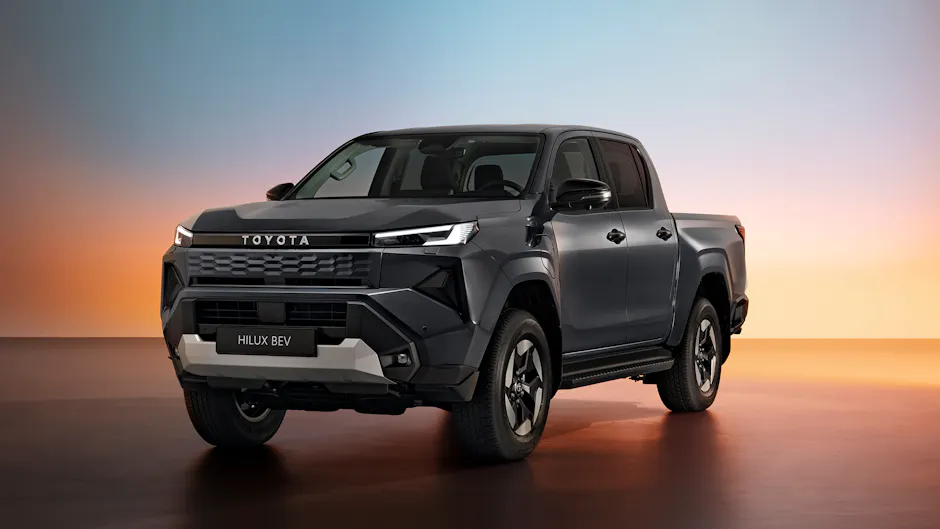 Front- und Seitenansicht des vollelektrischen Toyota Hilux in dunkelgrauer Lackierung vor farbigem Hintergrund.