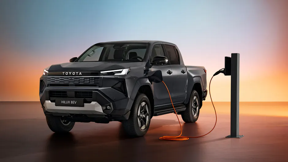 Toyota Hilux BEV beim Laden an einer Ladesäule mit orangefarbenem Ladekabel.