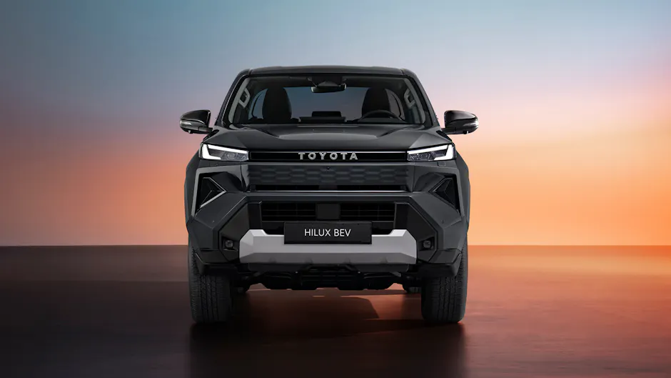 Frontansicht des vollelektrischen Toyota Hilux mit markantem Kühlergrill und LED-Scheinwerfern vor farbigem Hintergrund.
