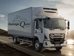 Weiss-grauer Isuzu-Lieferwagen mit grossem Aufbau und Logo «Garage Quici Kemptthal» fährt bei Sonnenaufgang auf einer Landstrasse.